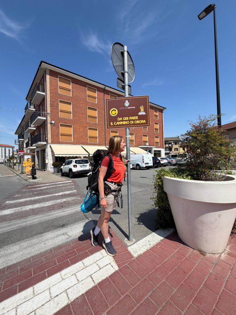 Eleonora con lo zaino accanto al cartello che segna la partenza del Cammino di Oropa