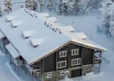 Cottage di legno col tetto innevato, visto dall'alto tra gli abeti